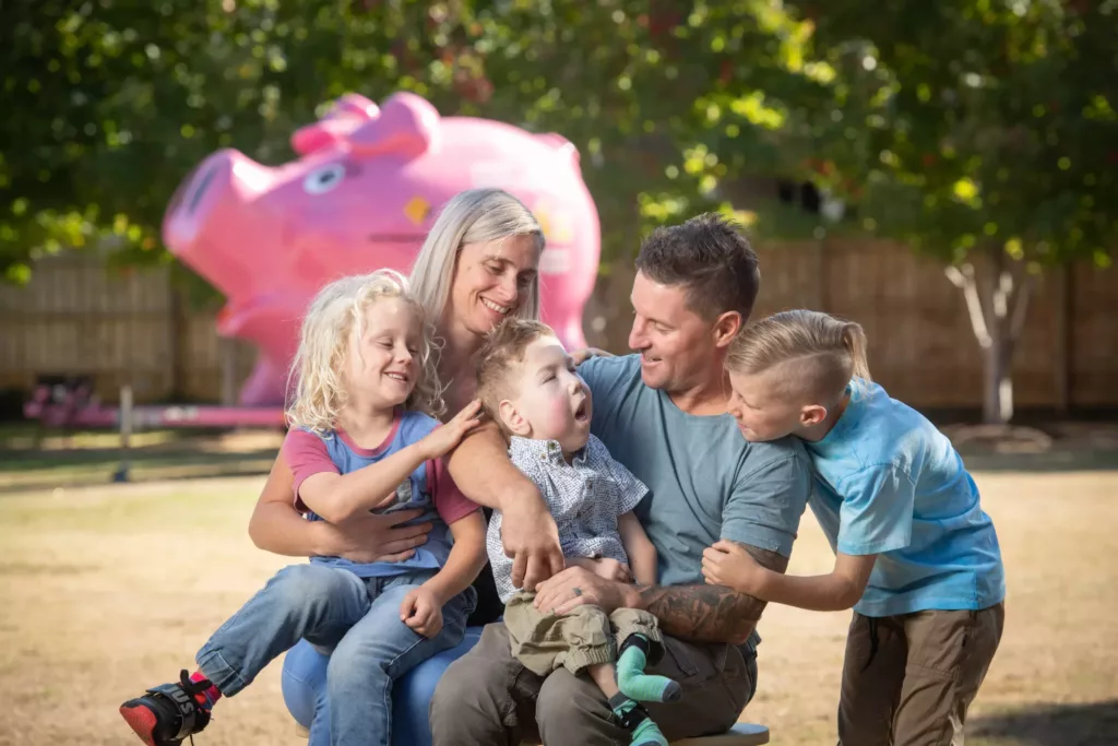 A family are sitting outside, smiling and laughing. There are two adults and three children.