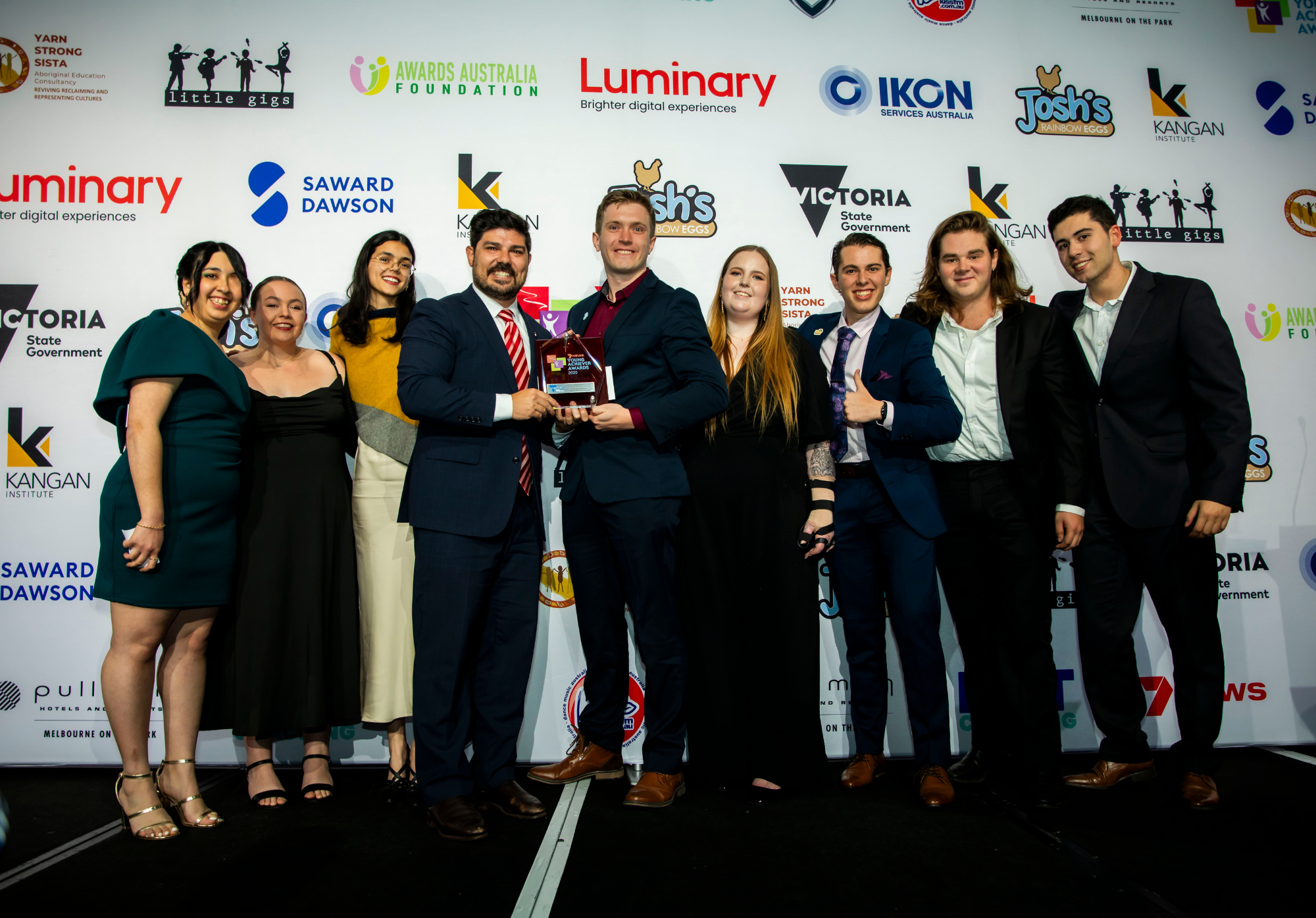 A group of young adults are standing on stage being presented a trophy