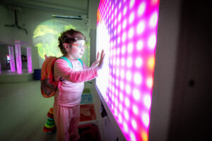 A girl is standing next to a coloured sensory screen