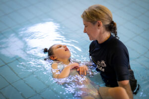 A woman helps a girl swim in a hydrotherapy pool