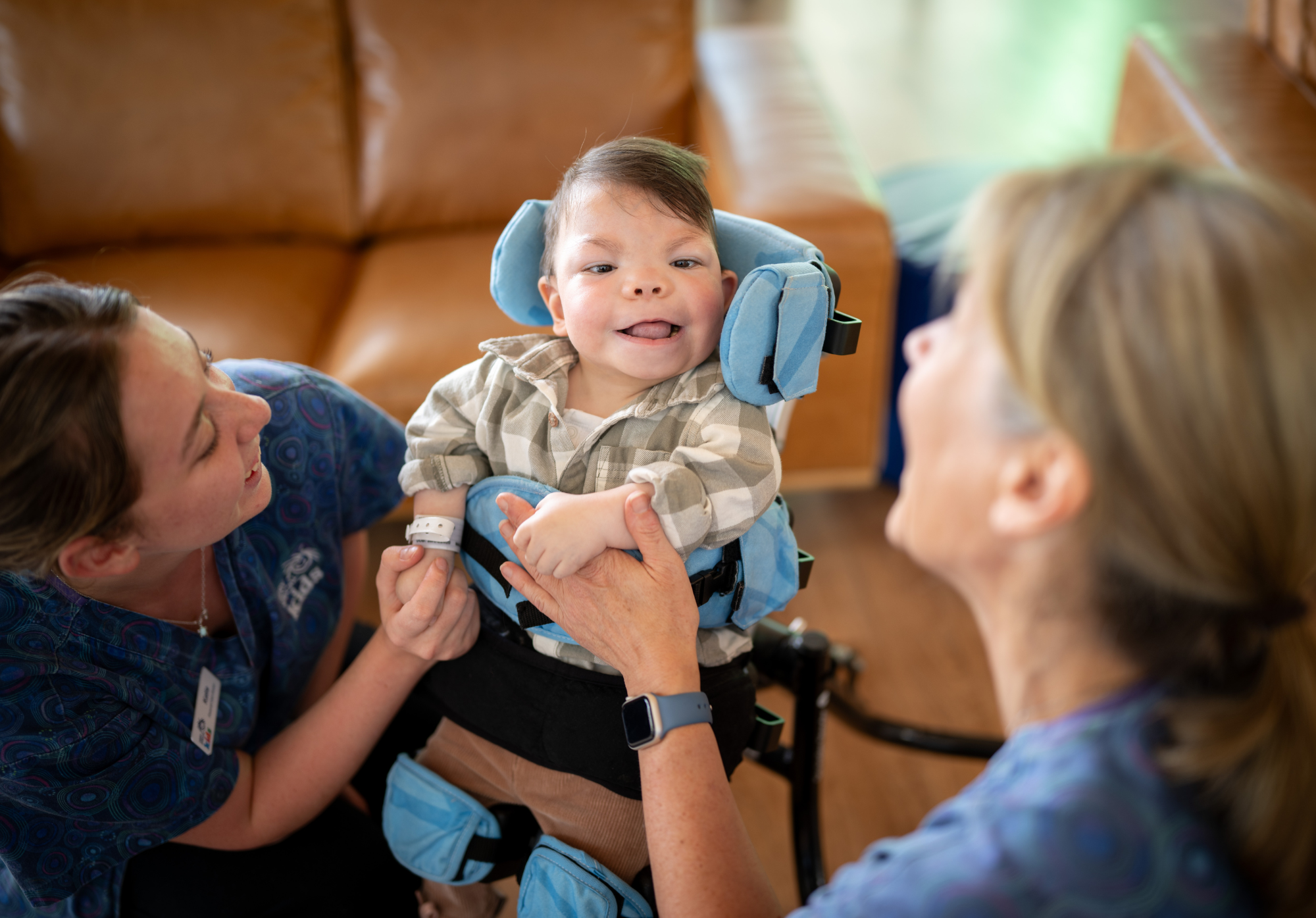A boy is smiling as he sits in a physio chair. There are nurses nearby.